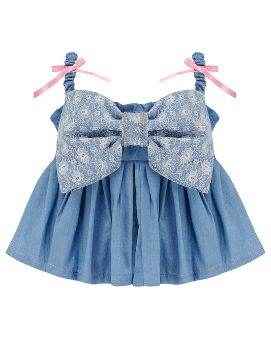 A denim crop top with a large white lace bow and diamante detail on the chest, pink topstitch elasticated shirring across the top bodice, and full babydoll gathered panel. It features elasticated shoulder straps with pink ribbon bow detail. Delta Of Phoenix Gigi Bow Top