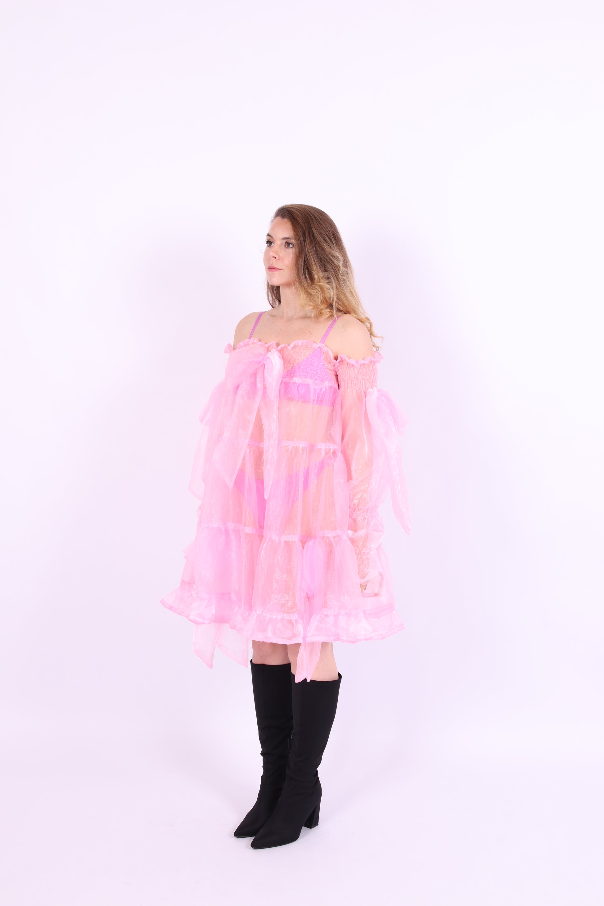 A bubblegum pink organza mini dress with a large bow detail at the sleeve, skirt, and front, featuring a bardot neckline and long puff sleeves. Cosette Dress by Delta Of Phoenix