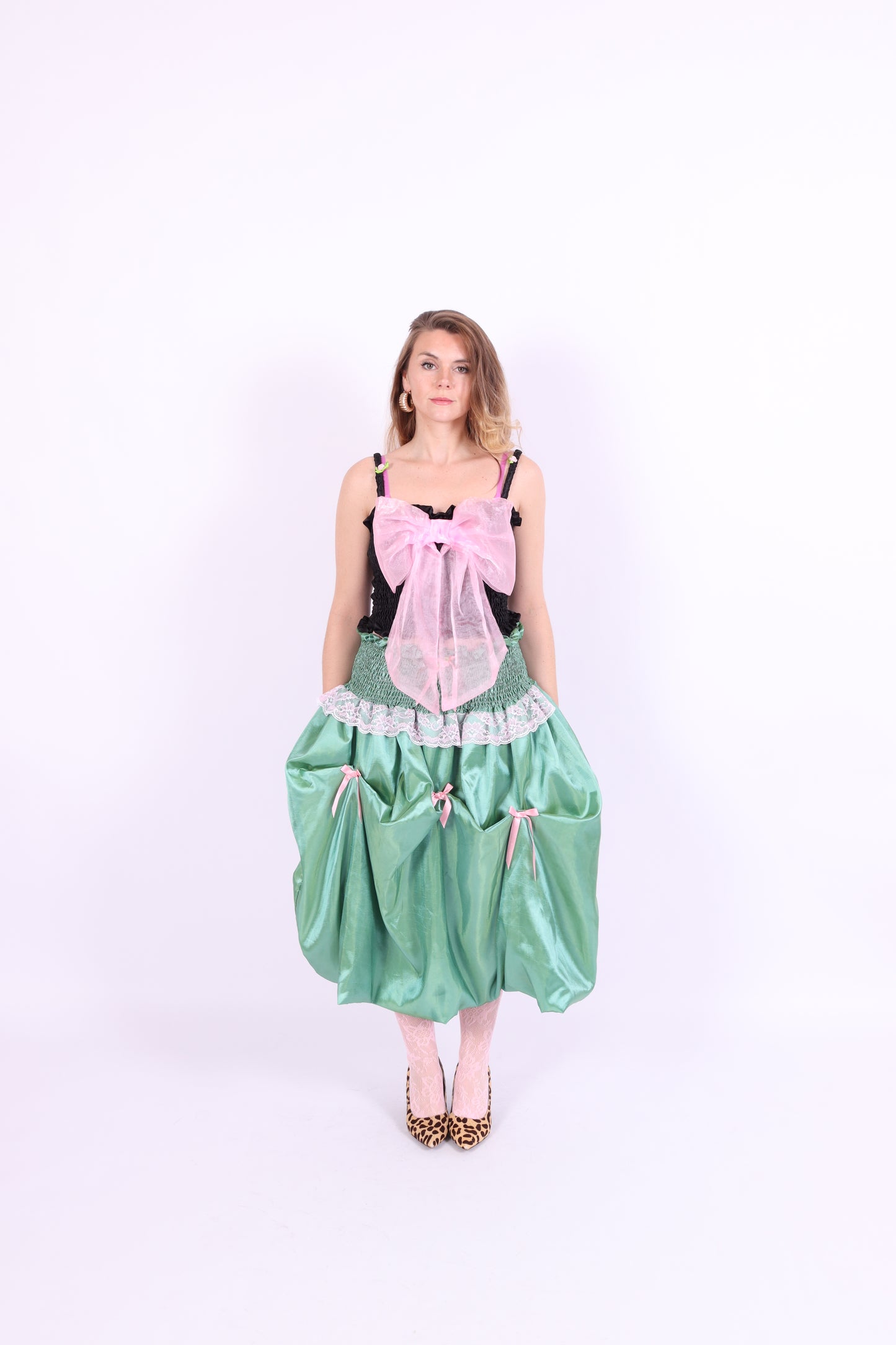 A black satin top with an elasticated shirring bodice and a large bubblegum pink organza bow on the front. It features elasticated shoulder straps with ruched detailing and is displayed against a plain background. Delta Of Phoenix Georgette Bow Top