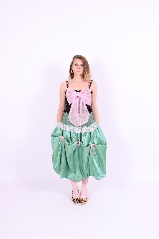 A black satin top with an elasticated shirring bodice and a large bubblegum pink organza bow on the front. It features elasticated shoulder straps with ruched detailing and is displayed against a plain background. Delta Of Phoenix Georgette Bow Top