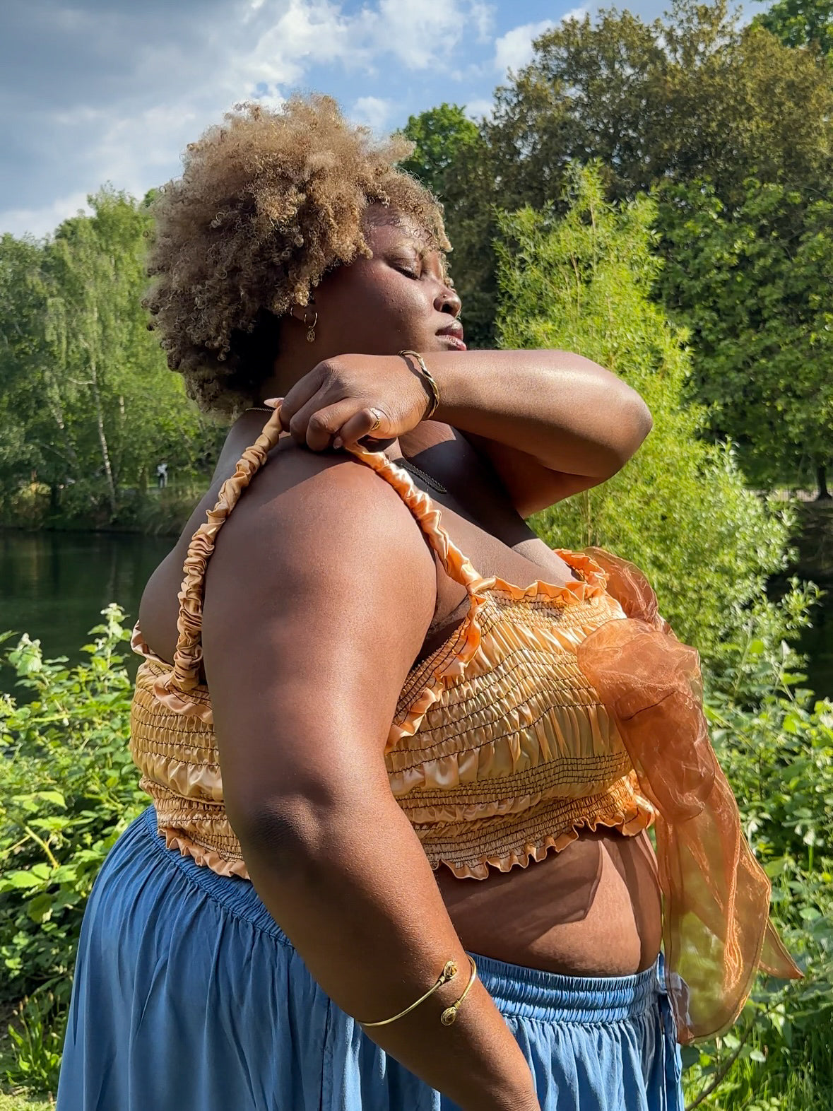 A gold satin top with an elasticated shirring bodice and a terracotta brown organza bow on the front. It features shoulder straps with elasticated and ruched details. Delta Of Phoenix Naomi Bow Top - worn by Naomi Native