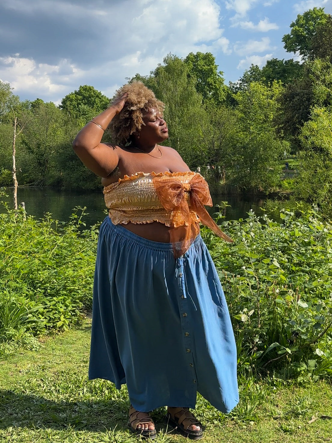 A gold satin top with an elasticated shirring bodice and a terracotta brown organza bow on the front. It features shoulder straps with elasticated and ruched details. Delta Of Phoenix Naomi Bow Top - worn by Naomi Native
