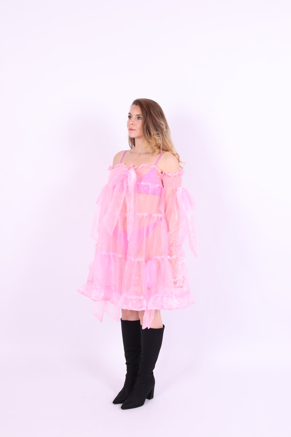 A bubblegum pink organza mini dress with a large bow detail at the sleeve, skirt, and front, featuring a bardot neckline and long puff sleeves. Cosette Dress by Delta Of Phoenix