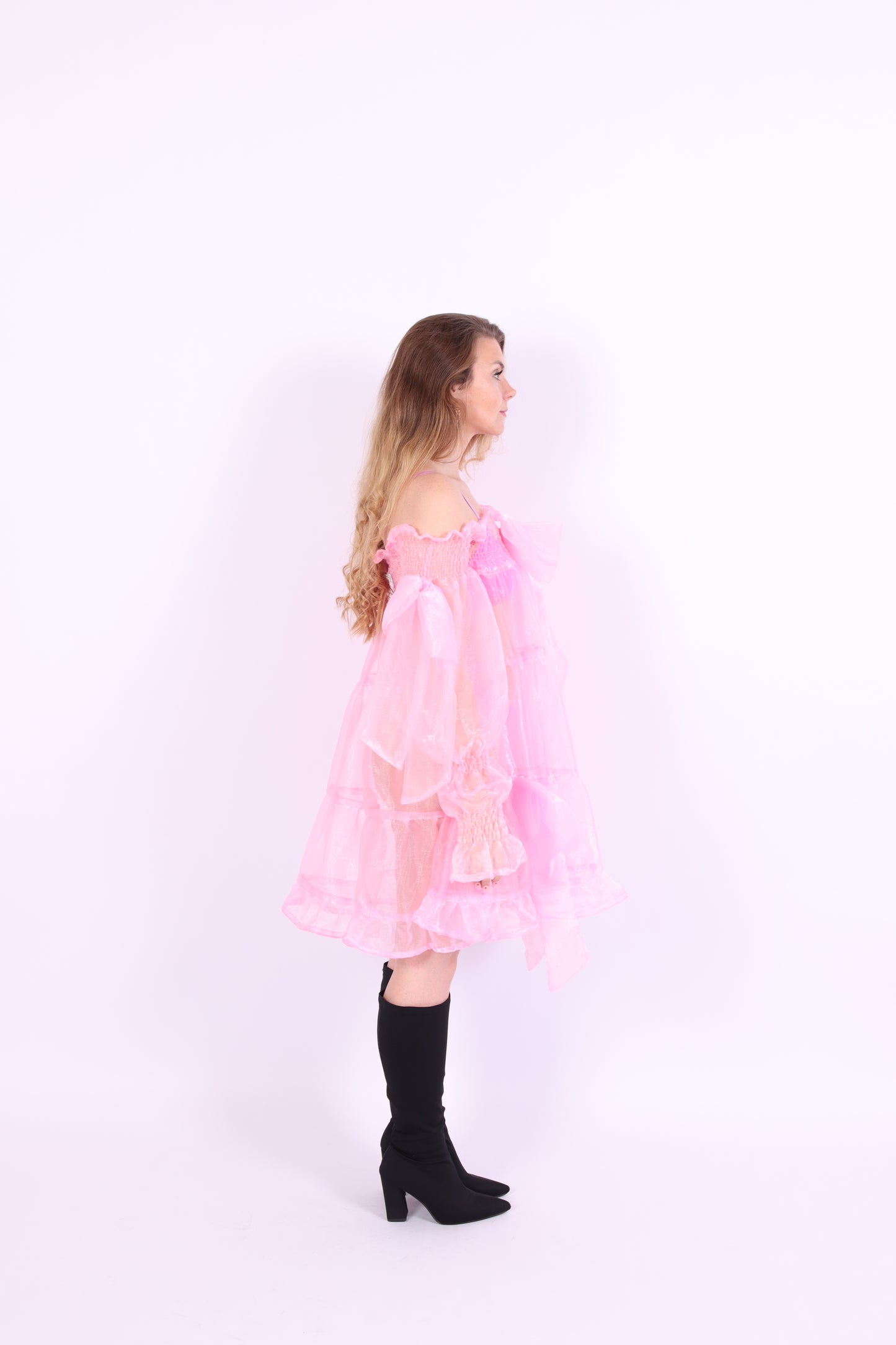 A bubblegum pink organza mini dress with a large bow detail at the sleeve, skirt, and front, featuring a bardot neckline and long puff sleeves. Cosette Dress by Delta Of Phoenix