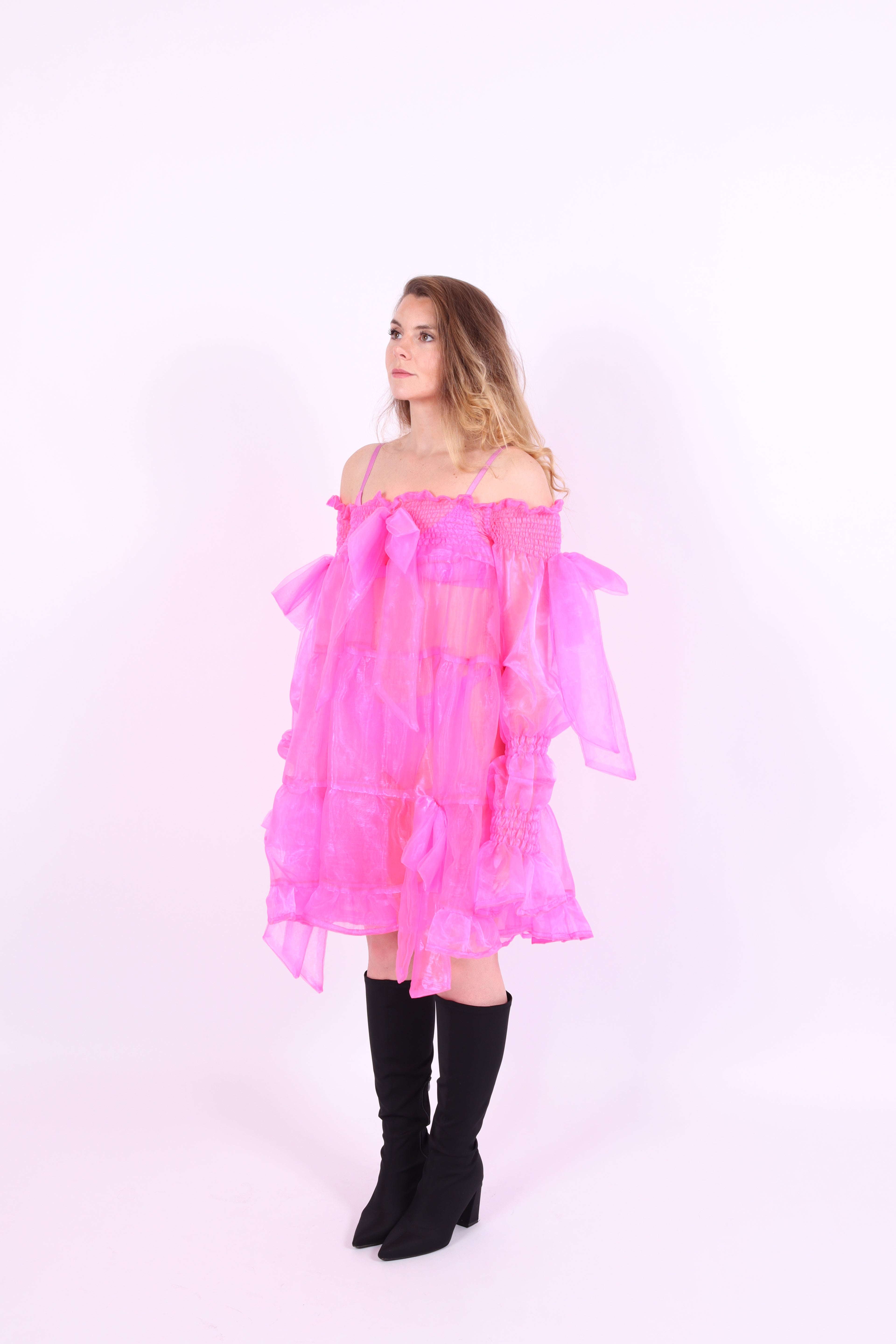 A neon pink organza mini dress with a large bow detail at the sleeve, skirt, and front, featuring a bardot neckline and puff sleeves. Delta Of Phoenix neon pink Cordelia dress