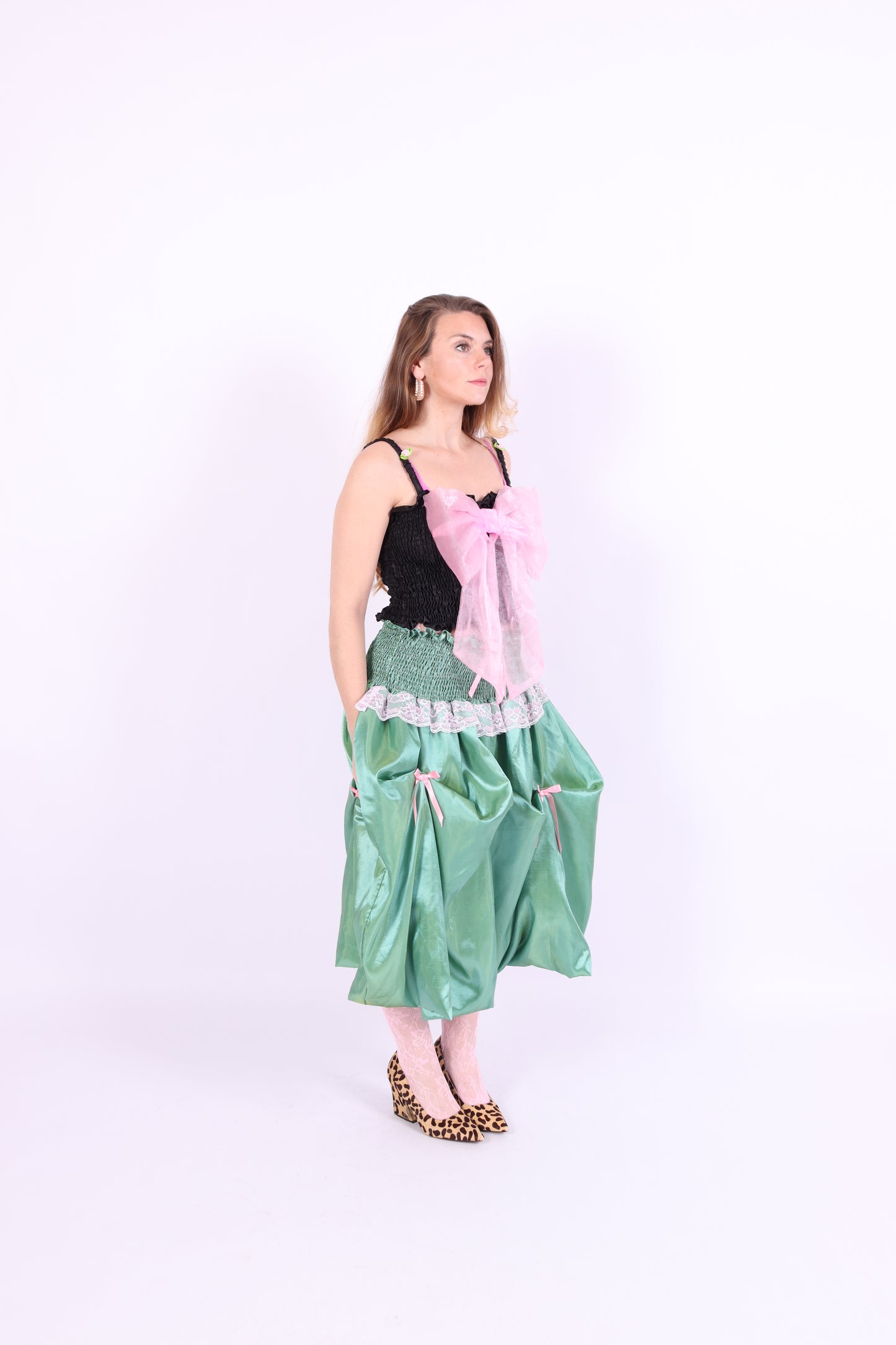 A black satin top with an elasticated shirring bodice and a large bubblegum pink organza bow on the front. It features elasticated shoulder straps with ruched detailing and is displayed against a plain background. Delta Of Phoenix Georgette Bow Top