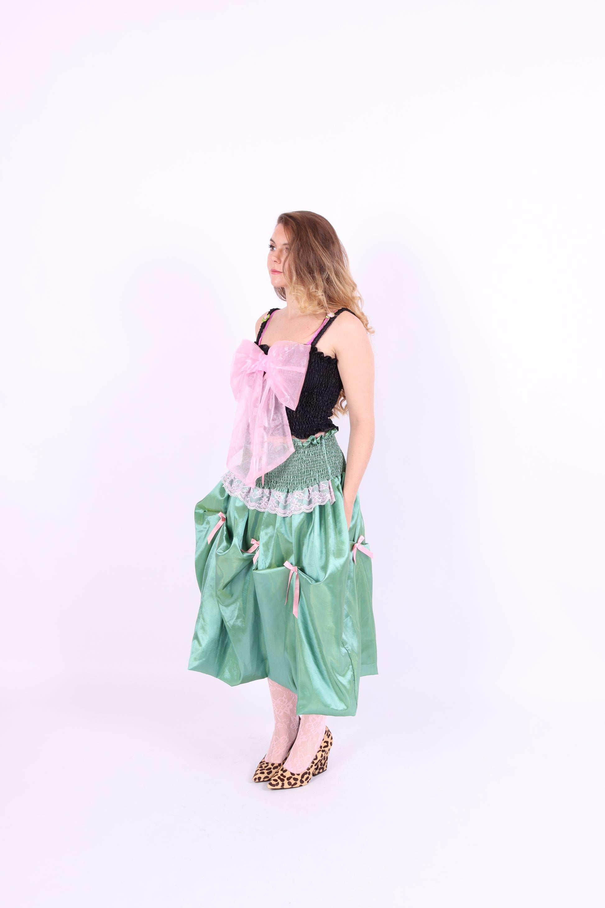 A black satin top with an elasticated shirring bodice and a large bubblegum pink organza bow on the front. It features elasticated shoulder straps with ruched detailing and is displayed against a plain background. Delta Of Phoenix Georgette Bow Top