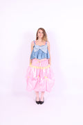 A denim crop top with a large white lace bow and diamante detail on the chest, pink topstitch elasticated shirring across the top bodice, and full babydoll gathered panel. It features elasticated shoulder straps with pink ribbon bow detail. Delta Of Phoenix Gigi Bow Top
