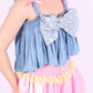 A denim crop top with a large white lace bow and diamante detail on the chest, pink topstitch elasticated shirring across the top bodice, and full babydoll gathered panel. It features elasticated shoulder straps with pink ribbon bow detail. Delta Of Phoenix Gigi Bow Top